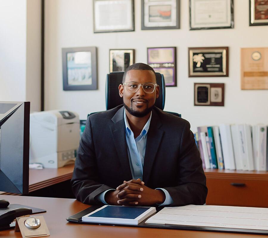 a faculty member sitting behind a desk smiling